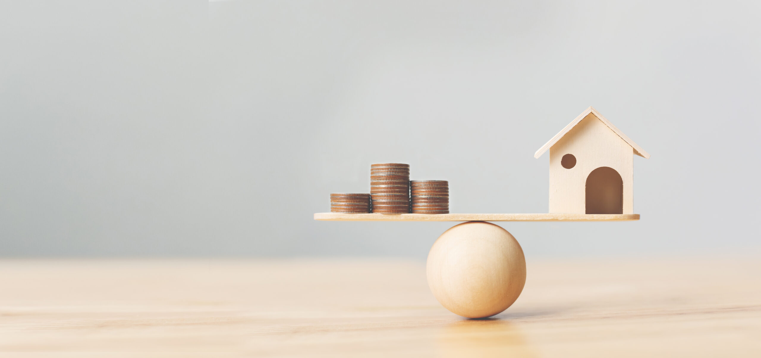 Wooden home and money coins stack on wood scale. Property investment and house mortgage financial real estate concept